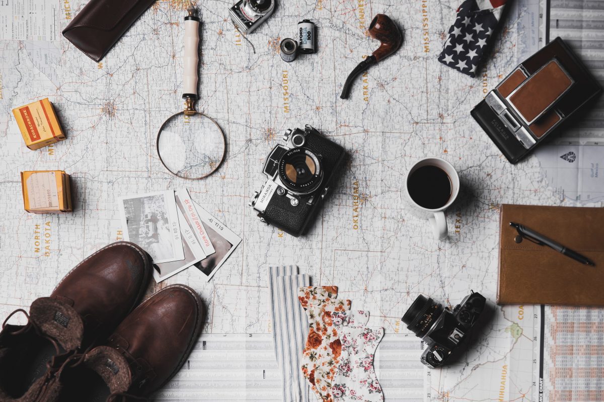 camera, leather shoes, magnifying glass, journals and other travel items on top of paper USA map
