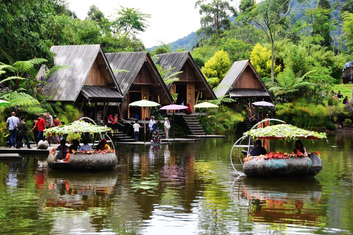 Floral boats float on a lake lined with huts on the edges in Dusun Bambu, Bandung, Indonesia